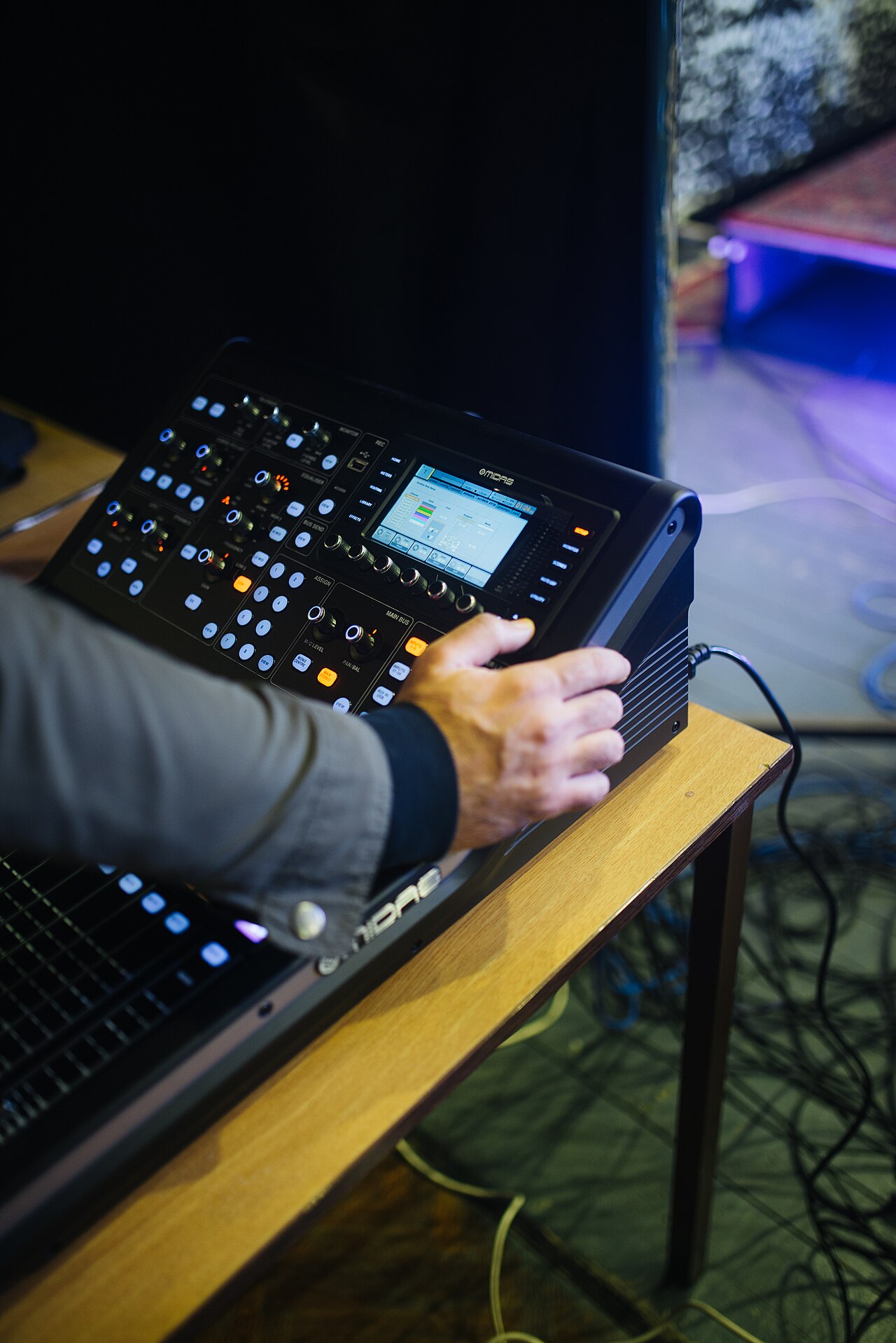 Sound engineer adjusting faders on a large mixing console during a live music performance.
